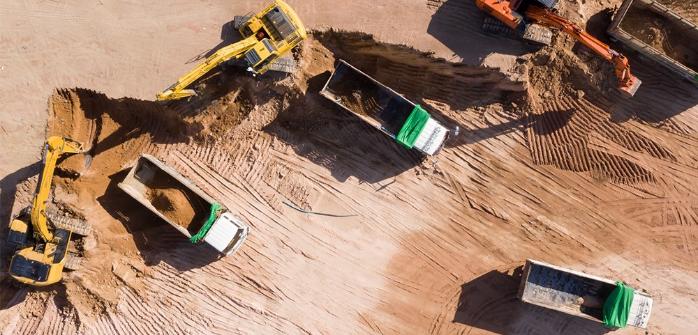An image of many cranes and commercial dump trucks from an aerial view. They're all parked in what looks like red clay. This represents Wolfspeed's products that support e-mobility projects on land.