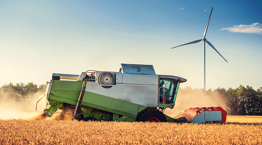 A electric powered tractor moves from the left to the right of the image. A modern white windmill is in the background.