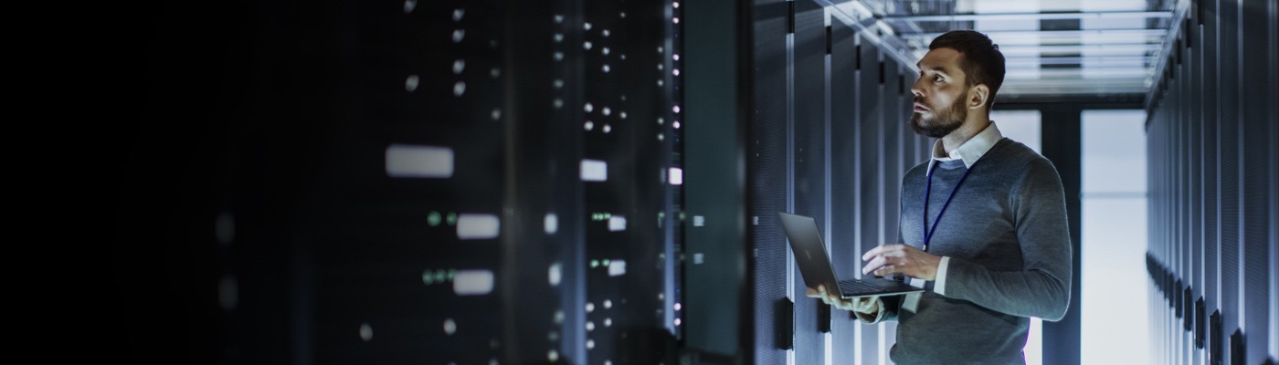 A man stands in front of a wall of databases and holds a laptop, representing career opportunities at Wolfspeed