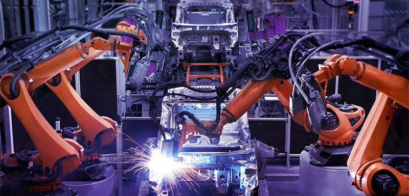 Image of robotic arms in a factory assembling cars. The robotic arms are driven by servo drives.